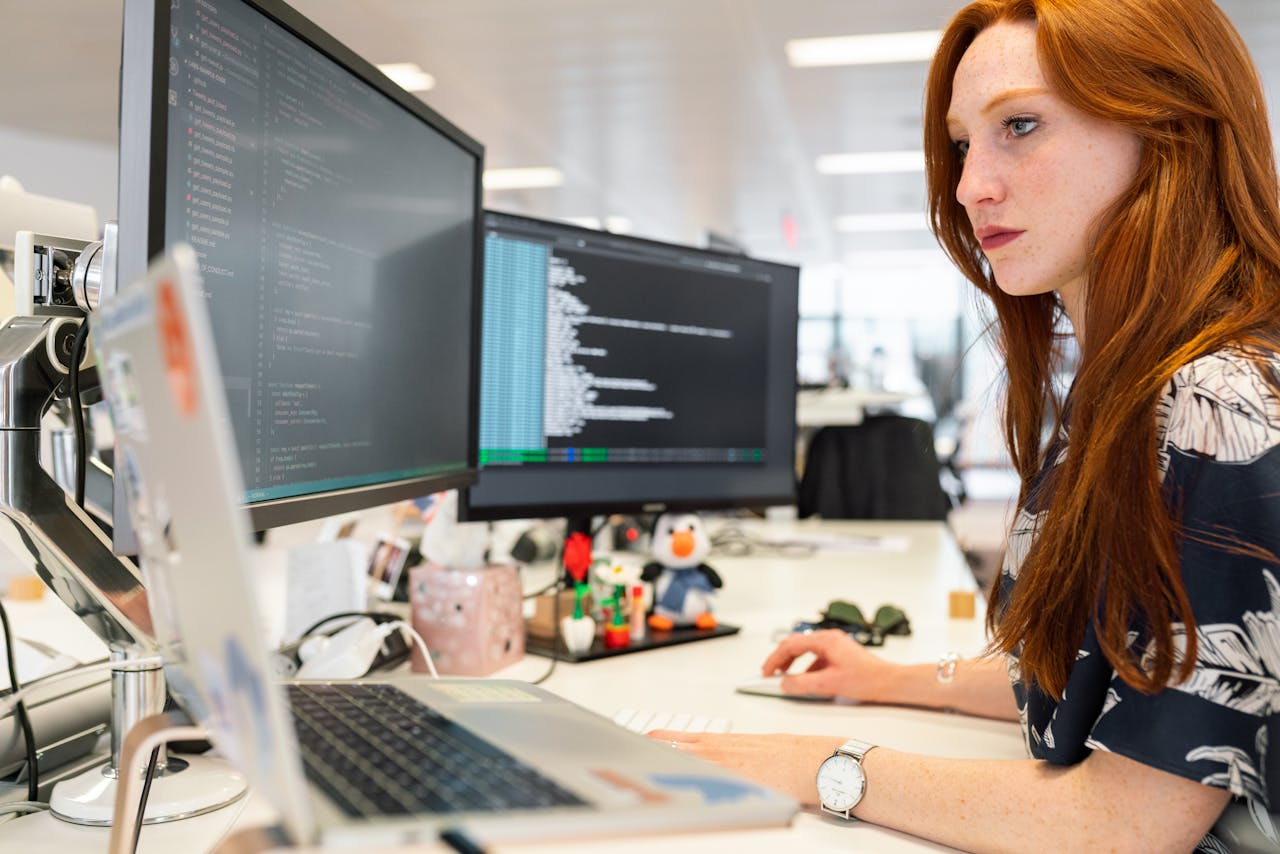 Home A focused female software engineer coding on dual monitors in a modern office.